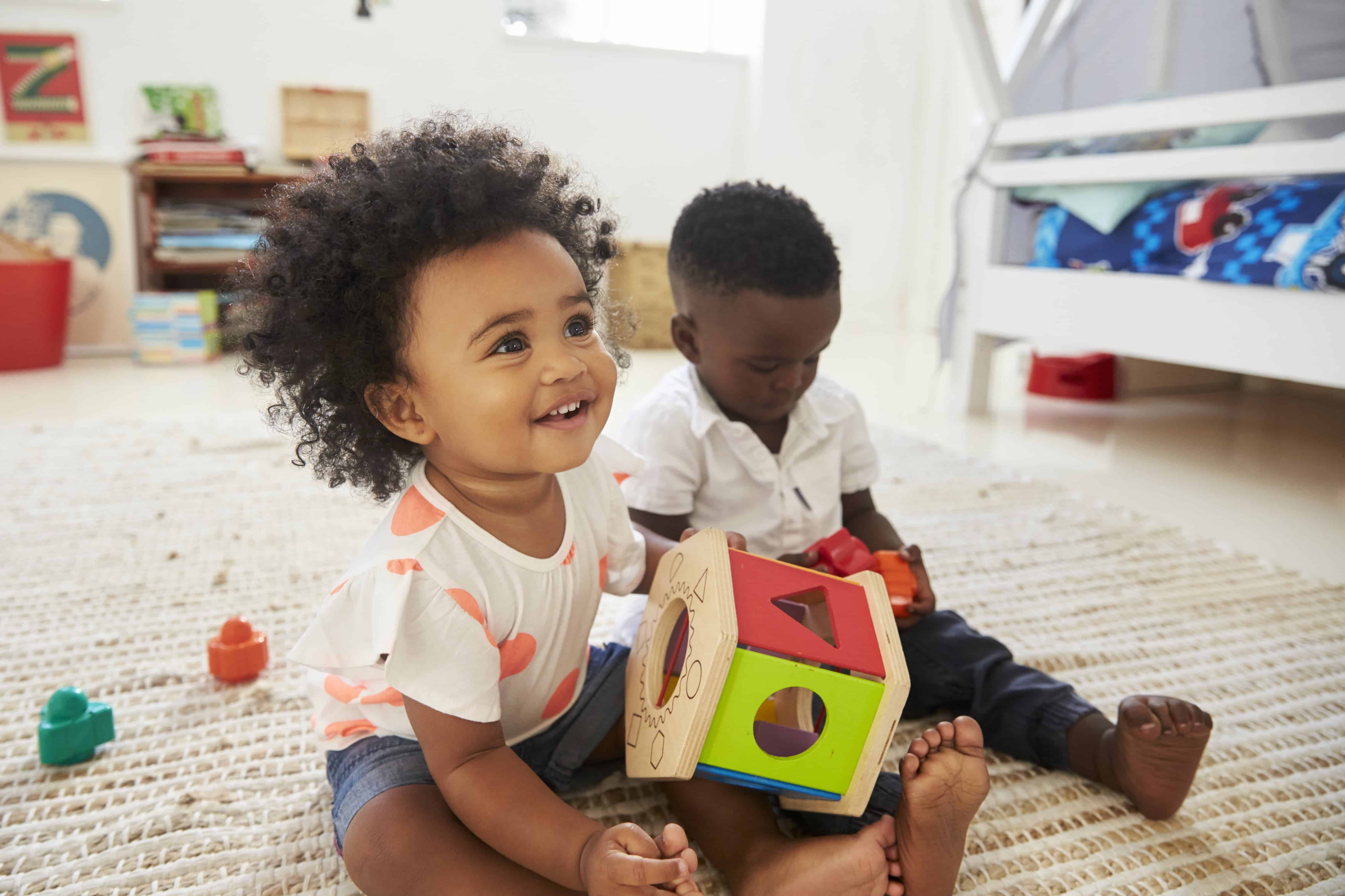 baby girl and baby boy playing with a wooden shape sorter.