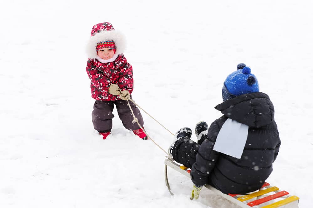Image of one child pulling another child in the snow on a sled.