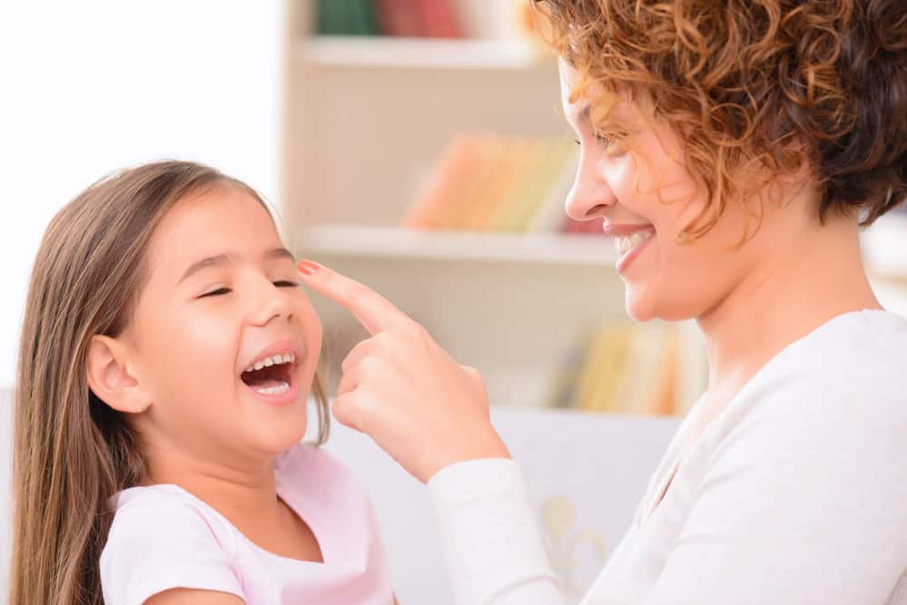 Mom and daughter playing a game where mom is pointing at daughter's nose.