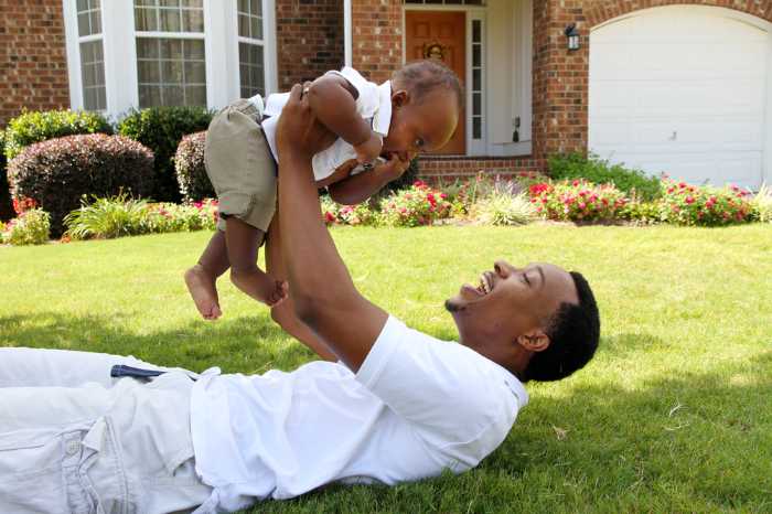 father holding up baby while laying on grass smiling