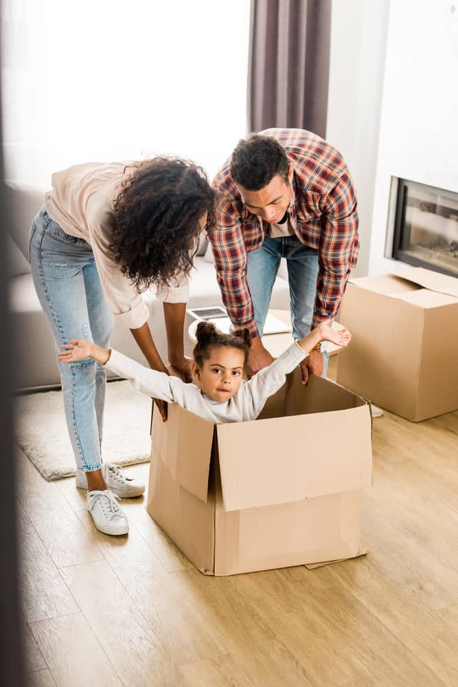 child playing in cardboard box with parents watching