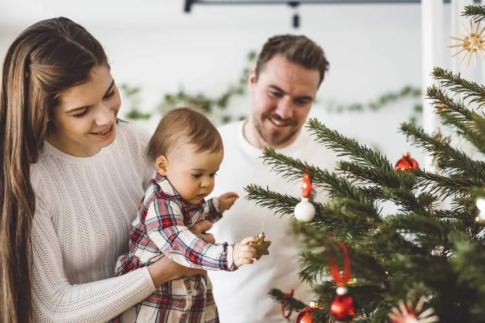 Happy young cheerful caucasian family of three mom dad and baby girl having fun decorating the Christmas tree. Family Christmas portrait.