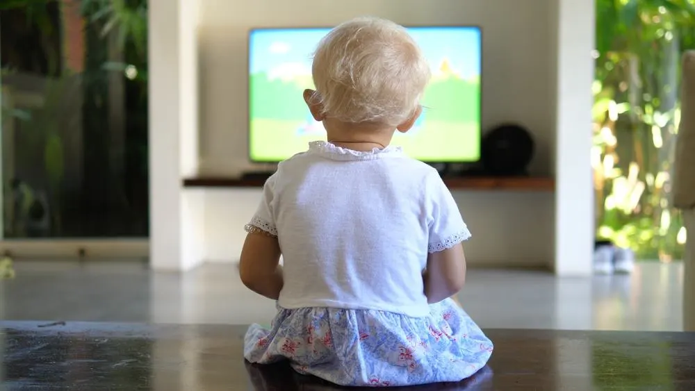 Back view of a little girl sitting on the floor watching the tv 