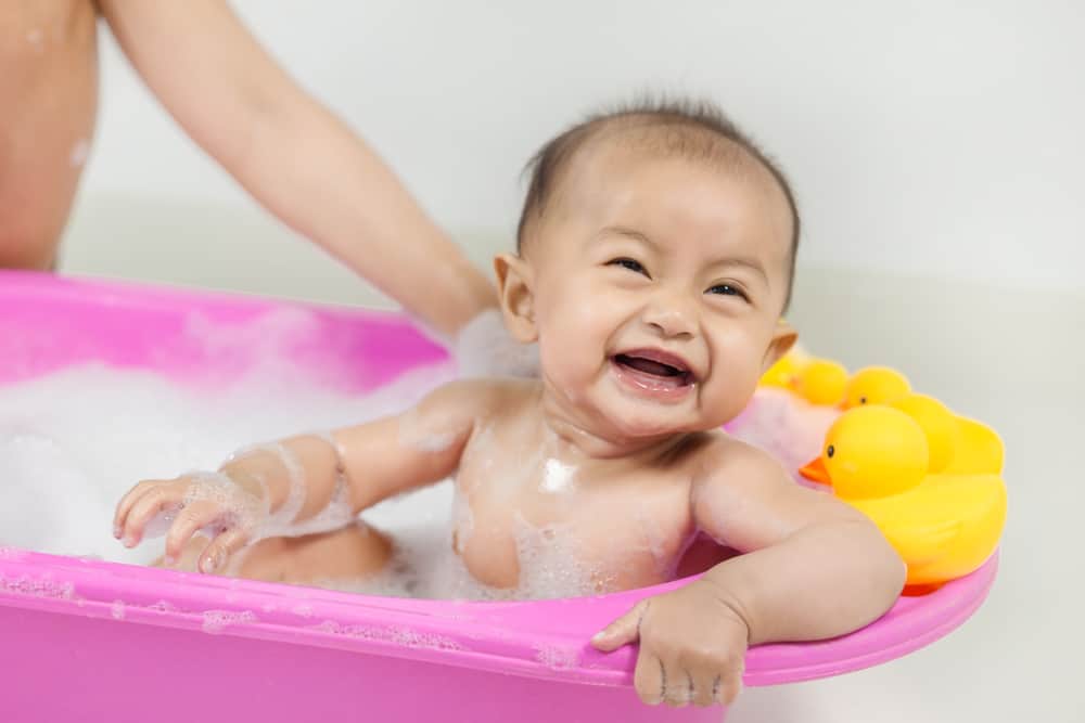 baby taking a bath in bathtub and playing with foam bubbles at home