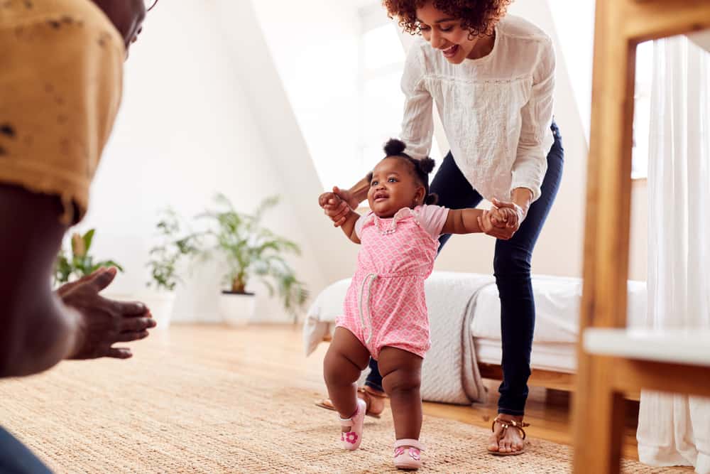 Parents At Home Encouraging Baby Daughter To Take First Steps