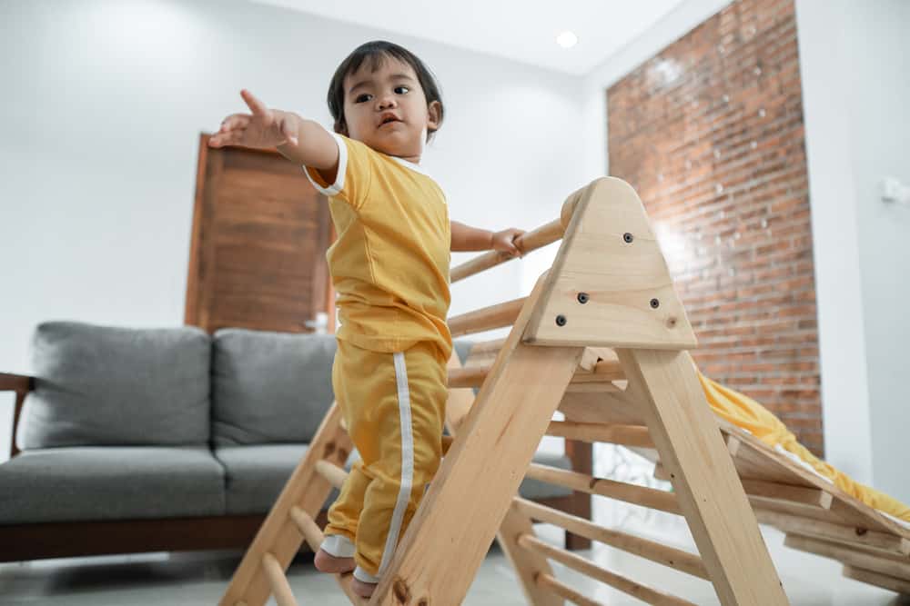 baby is afraid to reach out for help while climbing on the pikler triangle toy in the living room