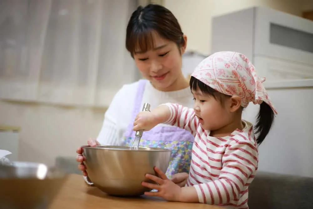 toddler stirring a whisk in a metal bowl with mom