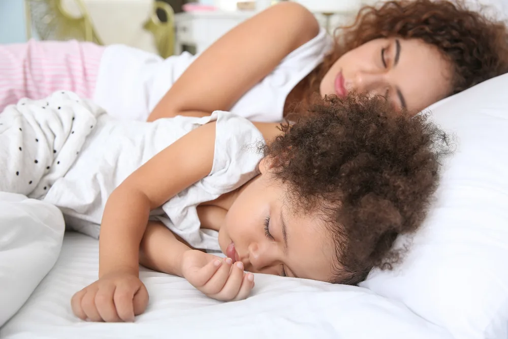 Little African-American girl with mother sleeping in bed