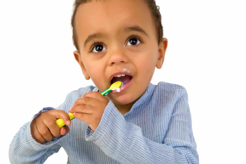 Smiling 18th month old African toddler boy brushing his teeth