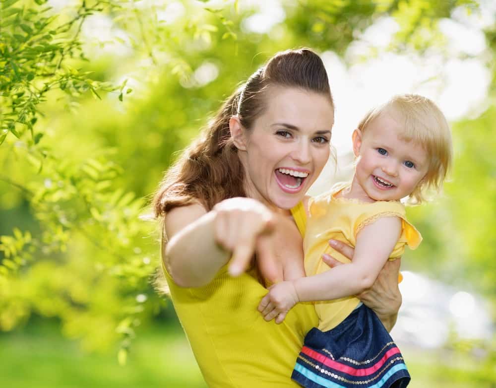 Portrait of baby girl and smiling mother pointing in camera