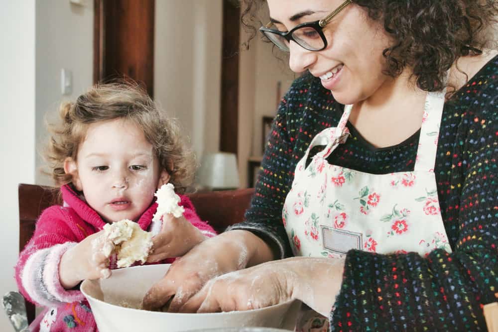 A young white Caucasian mother and daughter kneading dough for baking in a big white ceramic bowl