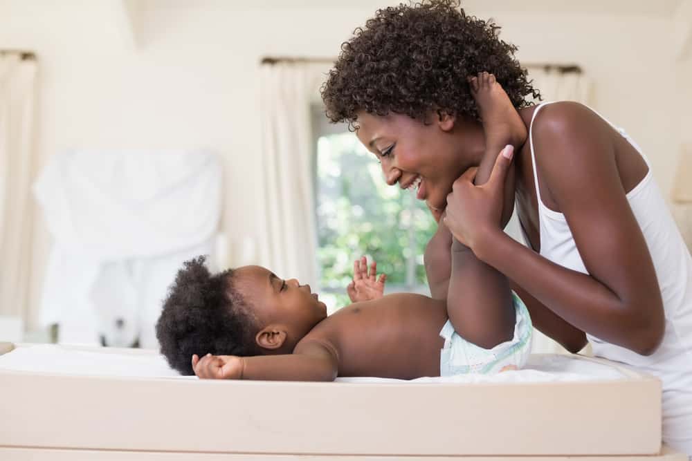 Happy mother with baby girl on changing table at home in the bedroom