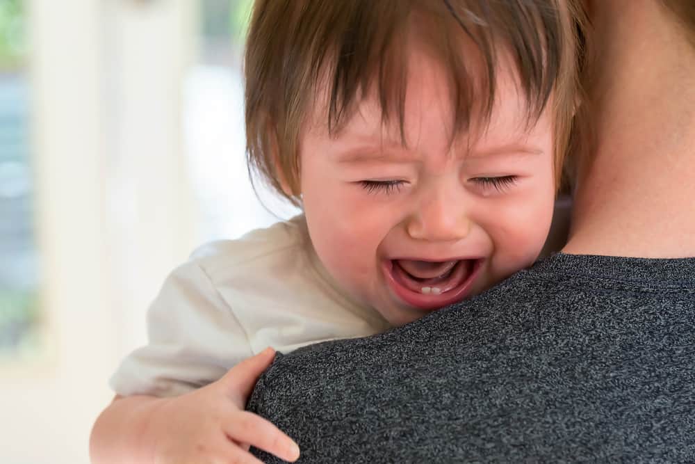 Upset toddler boy crying on his father's shoulder in his house
