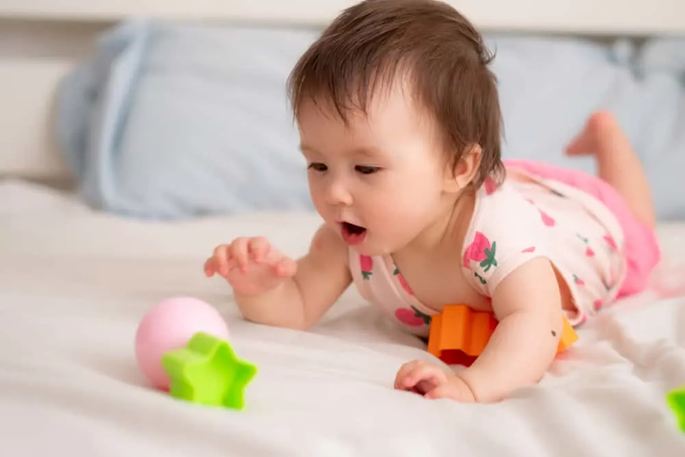 lifestyle home portrait of sweet and adorable mixed ethnicity Asian Caucasian baby girl playing with color blocks on bed excited and happy in childhood concept