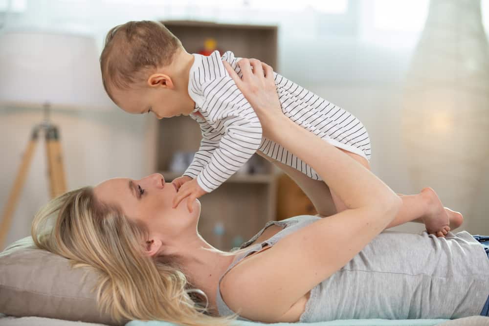 mother holding baby up in bed