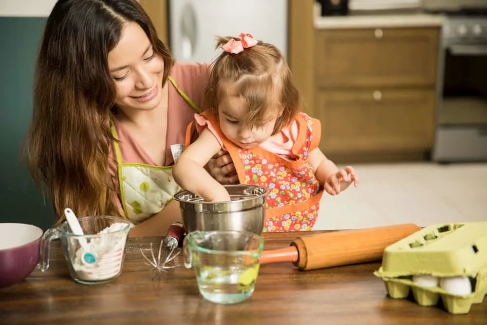 Good looking woman teaching her little cute girl to cook with some cookware in the kitchen