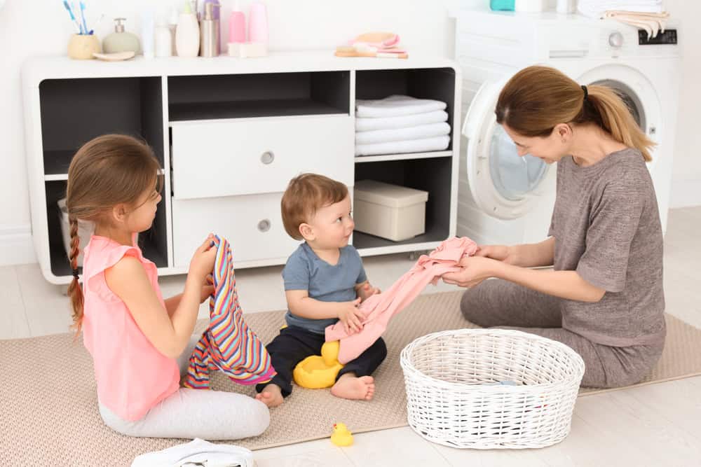 Housewife with children folding freshly washed clothes in laundry room