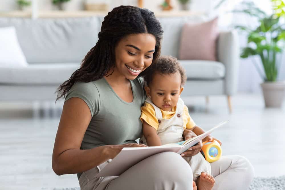 Caring African American Mommy Reading Book For Her Adorable Toddler Son At Home, Young Black Woman Bonding With Cute Little Infant Baby, Enjoying Spending Time Together, Closeup Shot With Copy Space