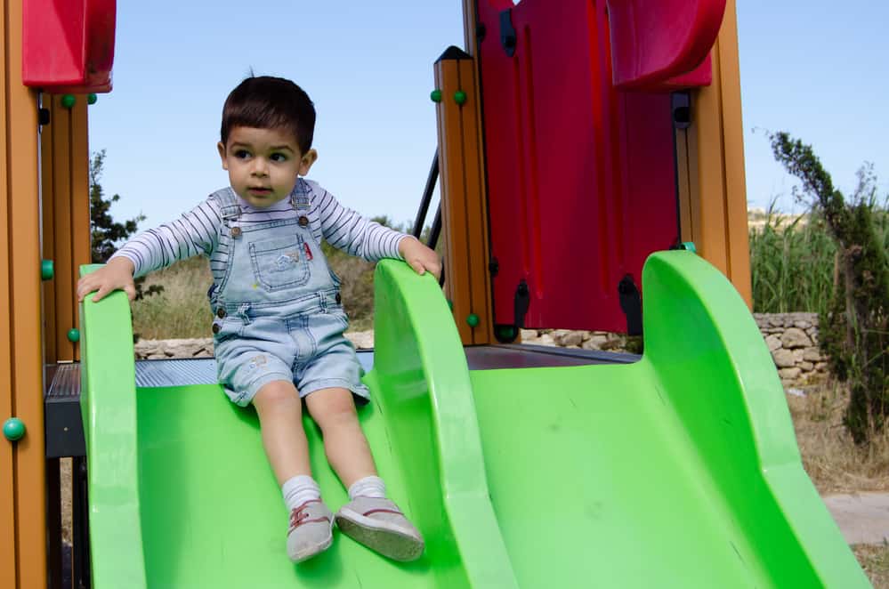 Cute two years old boy playing in the children playground outdoors on the slide.
