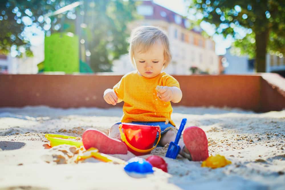 Adorable little girl having fun on playground in sandpit. Toddler playing with sand molds and making mudpies. Outdoor creative activities for kids